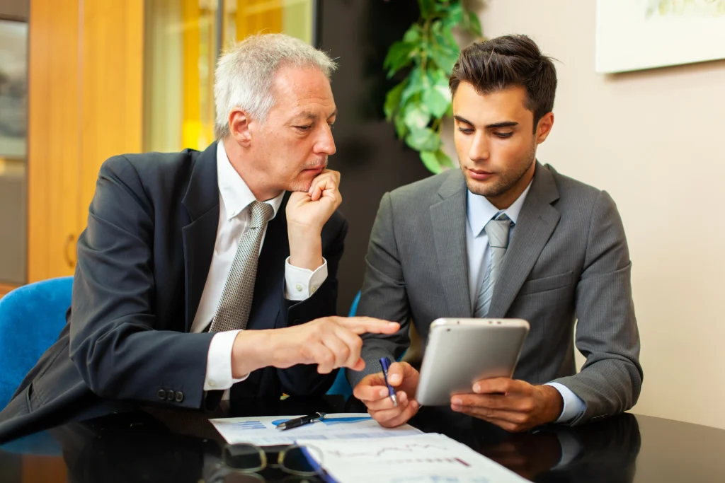 Two businessmen in suits reviewing financial data on a tablet during a meeting